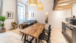 Et moderne køkken med et træbord og stole, et spiseområde med en sofa, og en trappe, der fører op til en etage.
