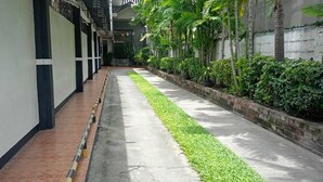 A narrow pathway flanked by greenery and a building with a tiled floor. - T'BOLI HOTEL (General Santos)