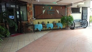 A hotel entrance with a wooden facade, a signboard, and a seating area with tables and chairs. - T'BOLI HOTEL (General Santos)