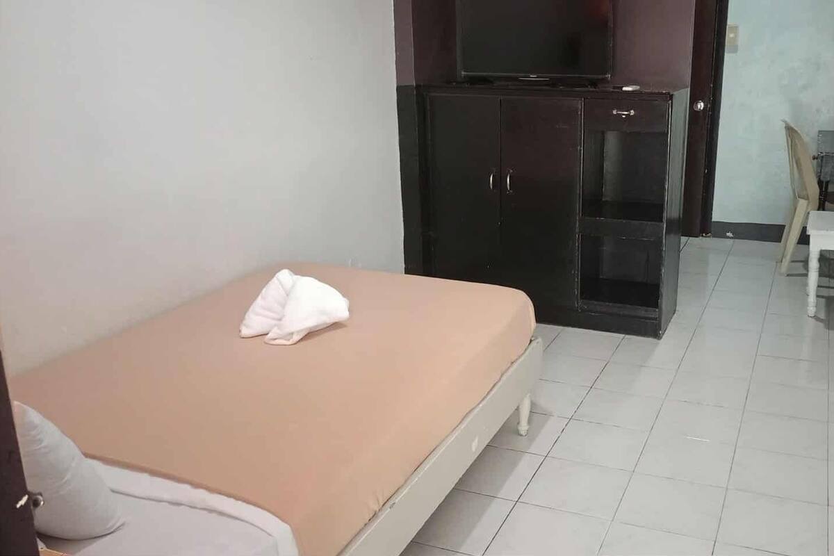 A small, simple room with a single bed, a wardrobe, and a desk.