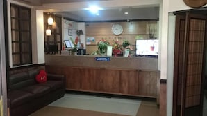 A reception area with a wooden counter, a clock, and a sign instructing to stand behind a line. - T'BOLI HOTEL (General Santos)