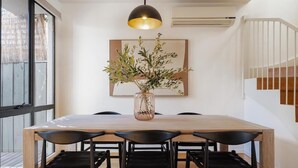A dining area with a wooden table, black chairs, a vase with greenery, and a pendant light.