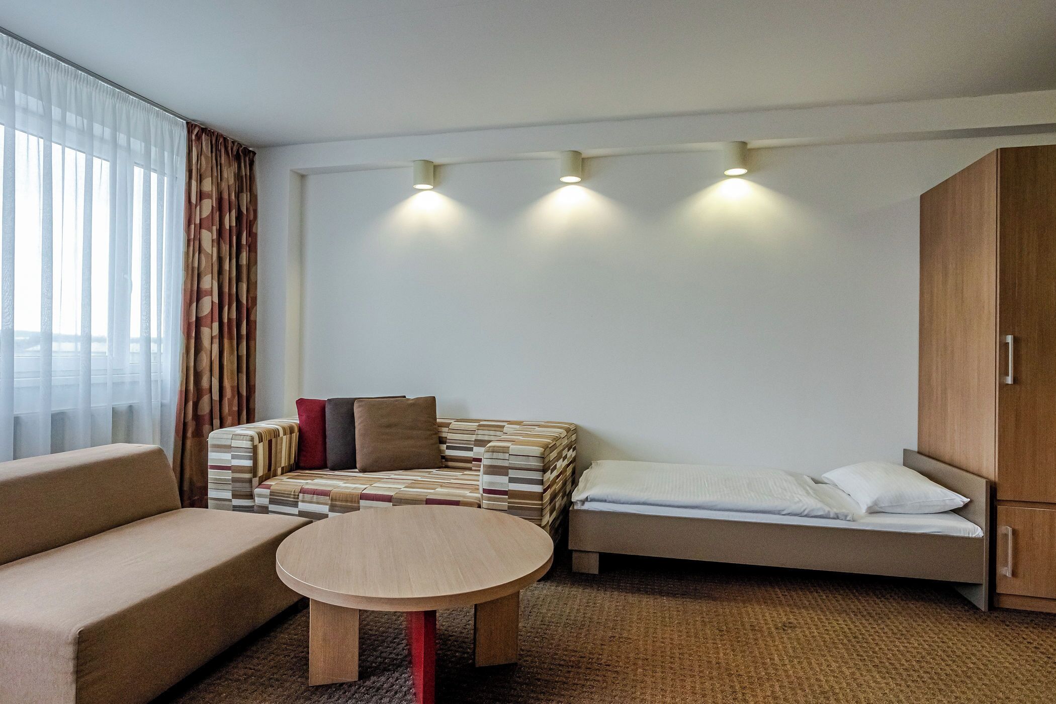 Quarto de hotel com sofá, uma mesinha redonda, cama e uma pilha de almofadas.