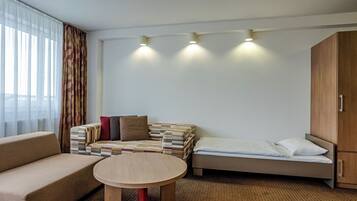 Quarto de hotel com sofá, uma mesinha redonda, cama e uma pilha de almofadas.