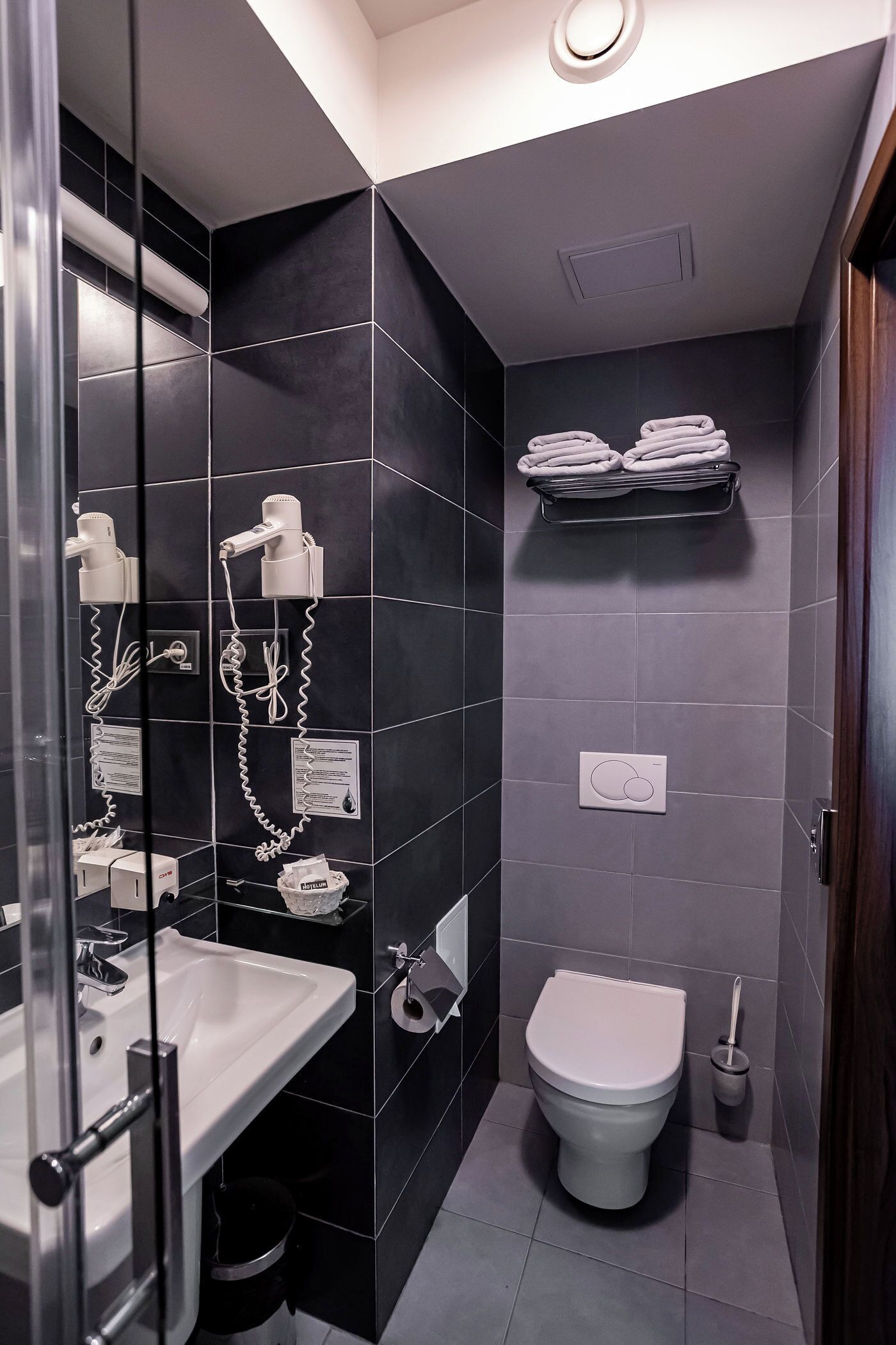 Et moderne badeværelse med en glasbrusekabine, en hvid vask, et toilet og en håndklædestige.