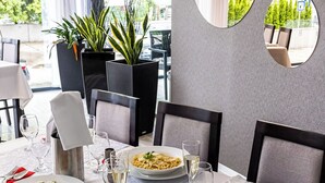 Een eetruimte met een tafel voor vier personen, compleet met pasta en salades, wijnglazen en een bloevas.