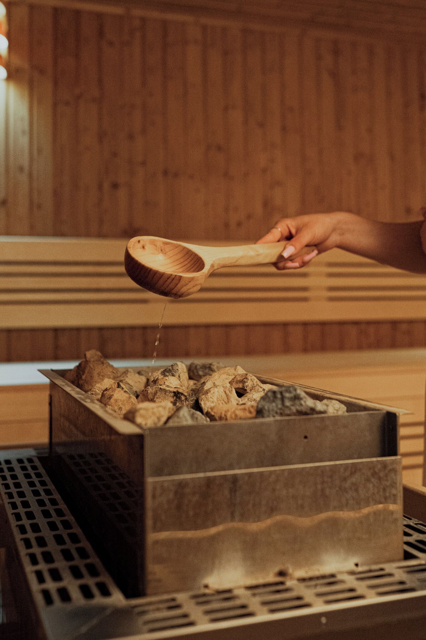 Ein Holzlöffel gießt Wasser in einen Metallbehälter mit Holzscheiten.
