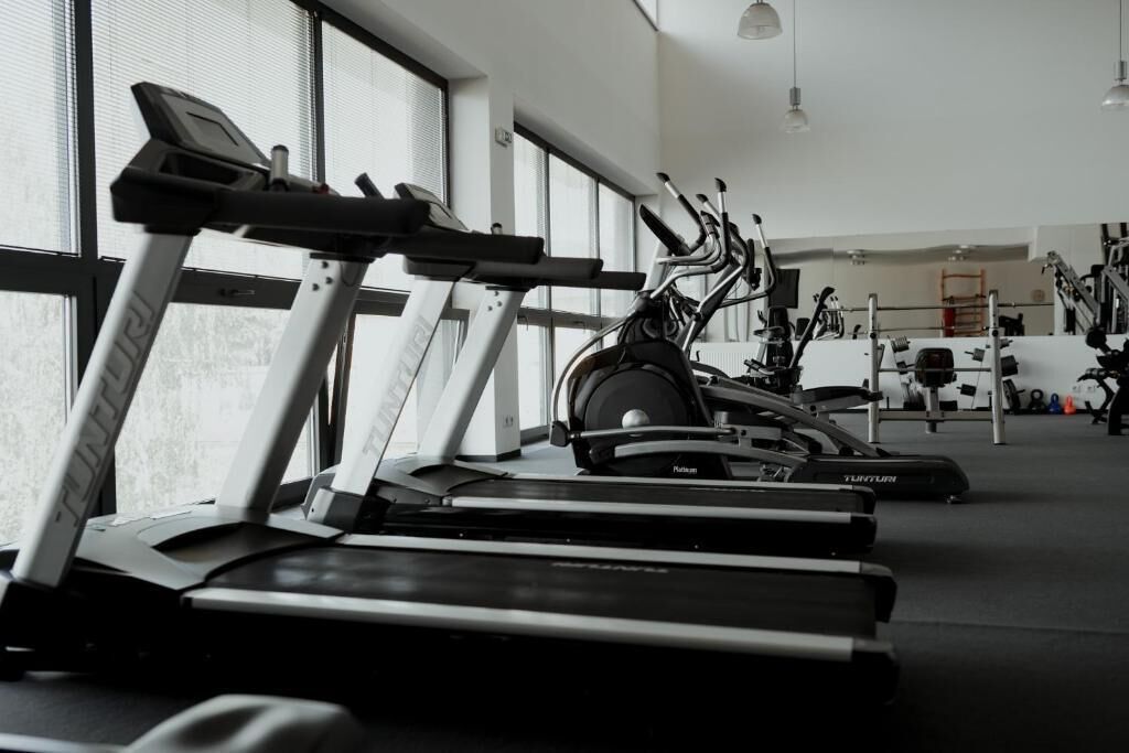 A gym with treadmills and stationary bikes, large windows, and various exercise equipment.