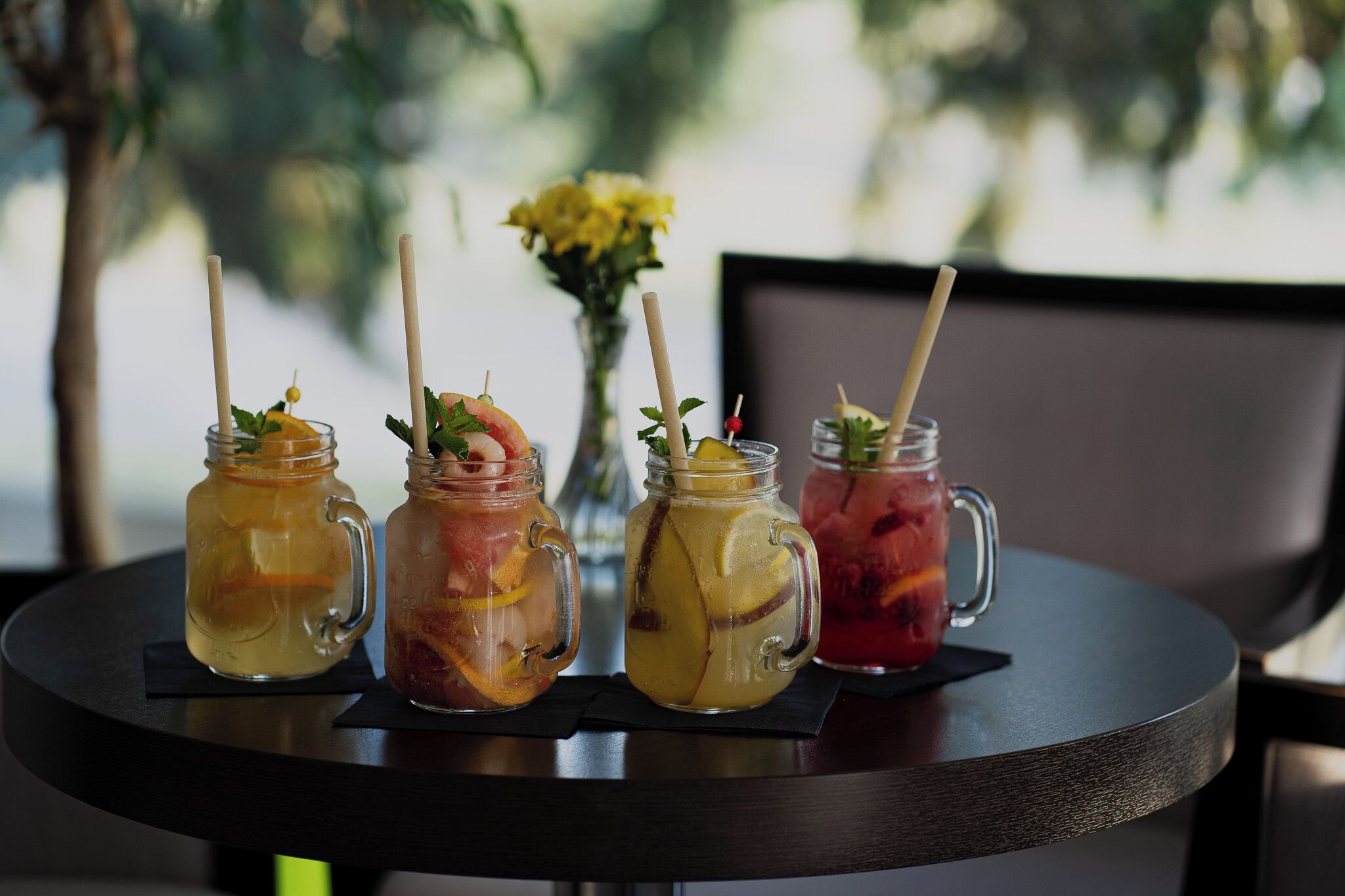 Four mason jars with straws and fruit on a table.