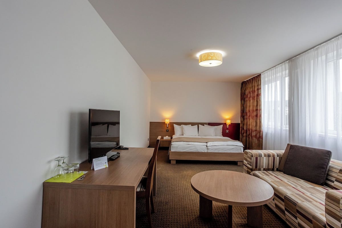 Una habitación de hotel con una cama, un sofá, un escritorio con una silla, una mesita y un televisor.