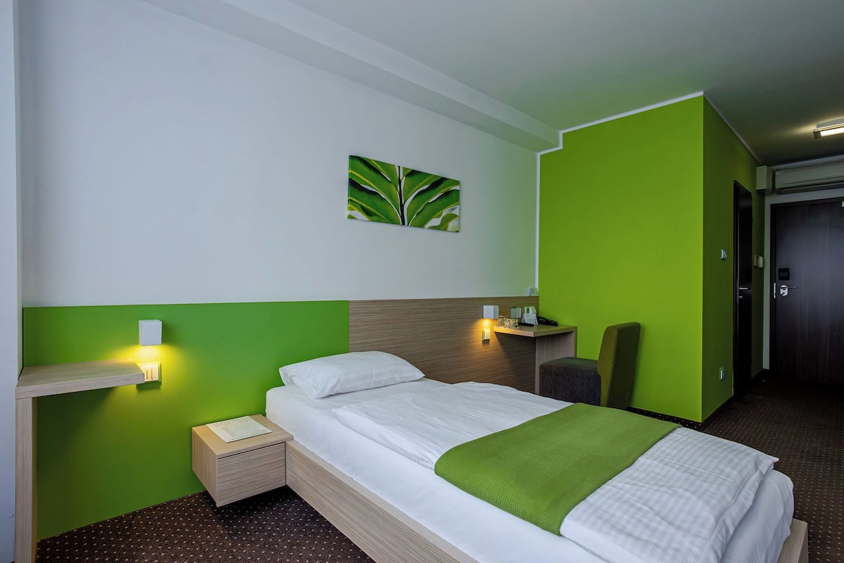 Una habitación de hotel con una cama, una mesita de noche, una pared verde, un cuadro y una silla.