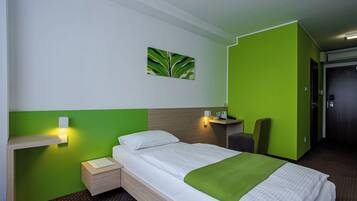 A hotel room with a bed, a nightstand, a green wall, a painting, and a chair.