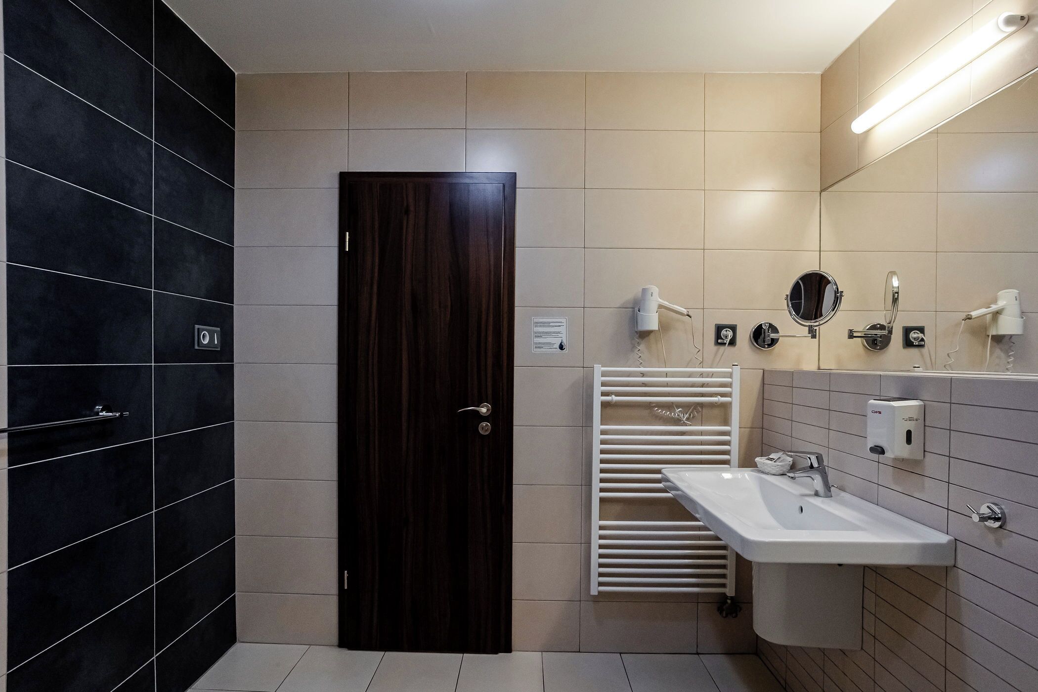 A modern bathroom with a dark wood door, a white sink with a mirror, and a towel rack.