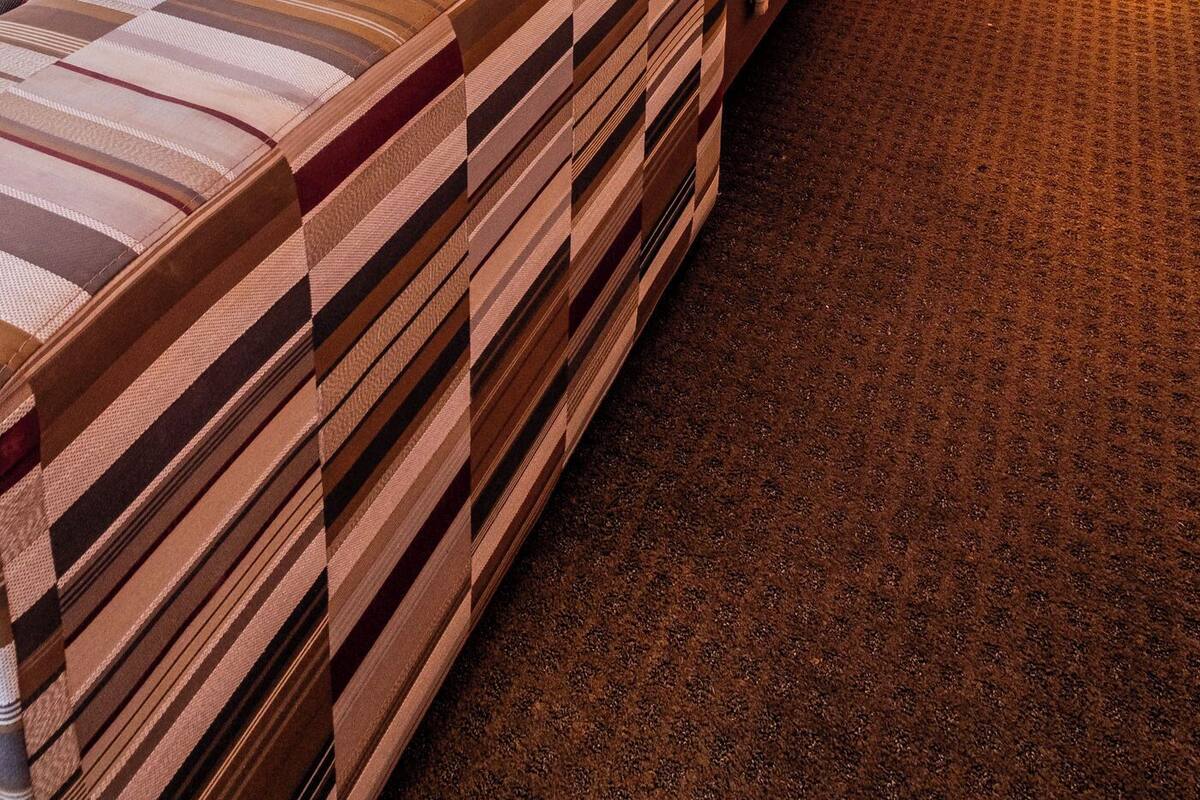 Una habitación de hotel con una cama, dos lámparas de noche, una mesita de noche y suelo alfombrado.