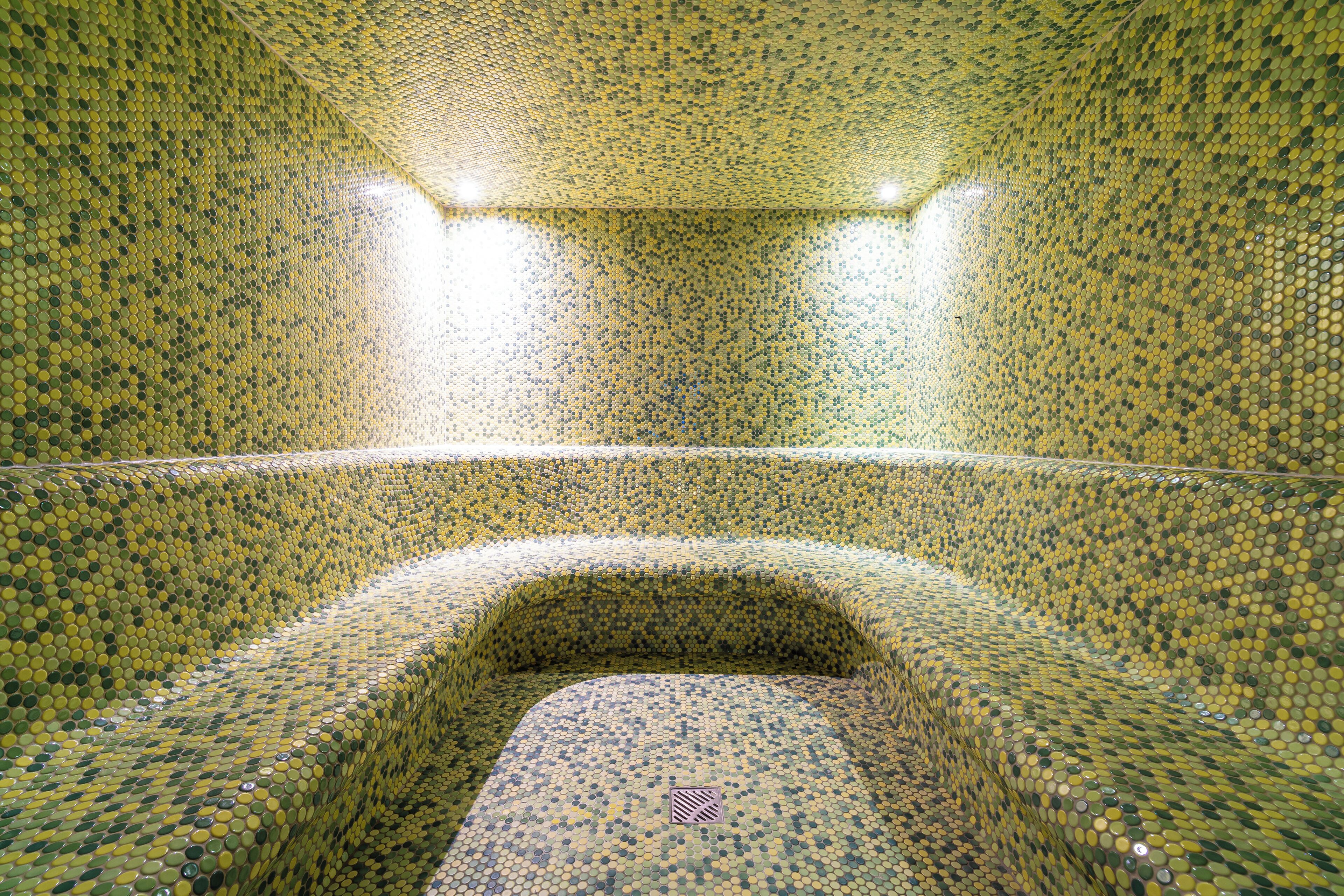 A room with a mosaic tiled floor and walls, a central seating area, and two overhead lights.