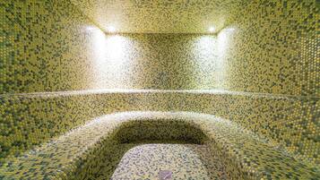 A room with a mosaic tiled floor and walls, a central seating area, and two overhead lights.
