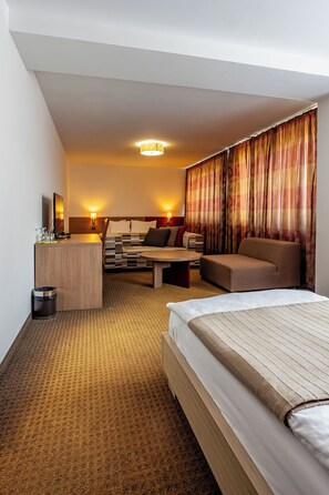 Habitación de hotel con cama, escritorio, sofá y una mesita. Hay un bote de basura y un televisor fijado a la pared.