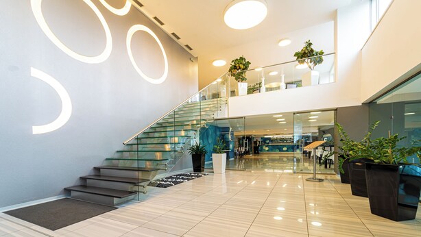 Een modern interieur met een glazen trap, een gepolijste vloer en potplanten.
