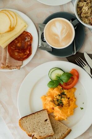 Un desayuno con huevos revueltos, tostadas, una taza de café y un plato con rodajas de tomate y pepino.