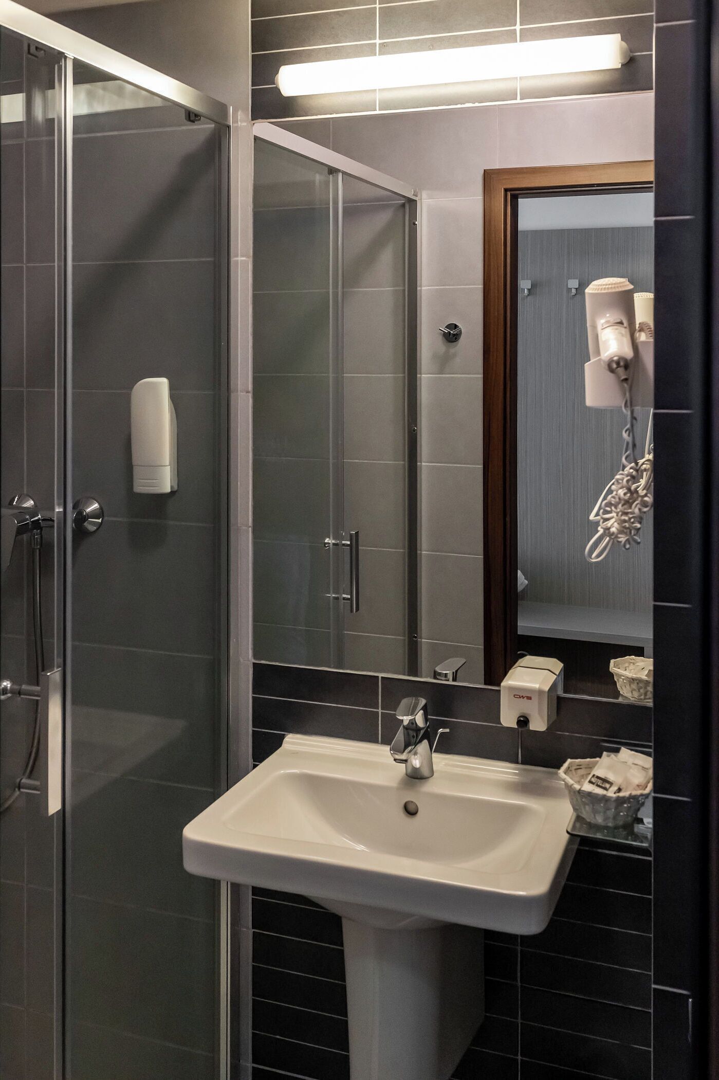 Un baño moderno con cabina de ducha de vidrio, un lavamanos blanco y un espejo con secador de pelo.