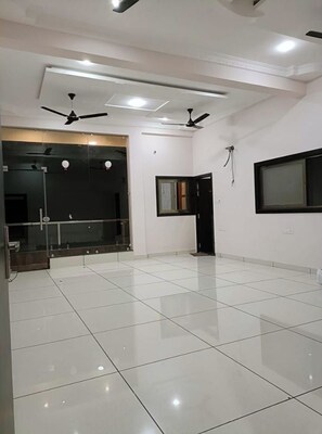 Una habitación amplia con piso de baldosas, ventiladores de techo, iluminación empotrada y un gran ventanal.