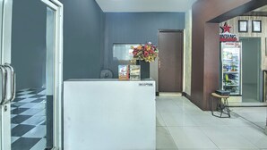A reception area with a reception desk, a flower vase, a refrigerator, and a small table with a chair. - OYO 94781 Hotel Lucky Inn Makassar (Makassar)