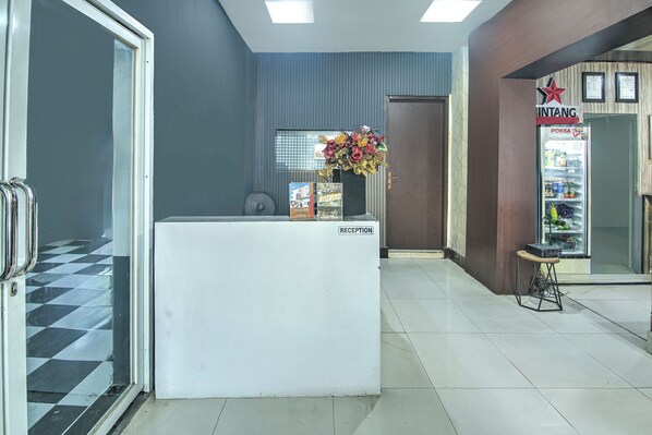 A reception area with a reception desk, a fan, a refrigerator stocked with beverages, and a flower arrangement. - OYO 94781 Hotel Lucky Inn Makassar (Makassar)