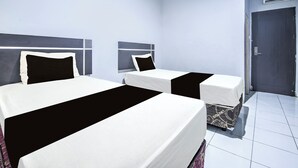 A hotel room with two beds, each with a white bedspread and black headboard. There is a small table with a patterned tablecloth and a chair. The room has a tiled floor and a door with a dark frame. - OYO 94781 Hotel Lucky Inn Makassar (Makassar)