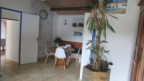 A room with a dining area featuring a round table and chairs, a clock on the wall, and a potted plant. - Longère vendéenne (Saint Hilaire de riez)