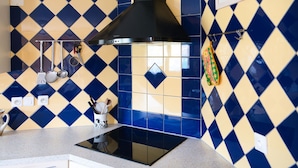 Une cuisine avec des carreaux bleus et jaunes formant un motif losangique, une hotte noire et des ustensiles de cuisine accrochés au mur.