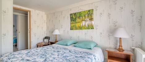 A bedroom with a bed, two bedside tables with lamps, a wall-mounted painting, and a radiator.