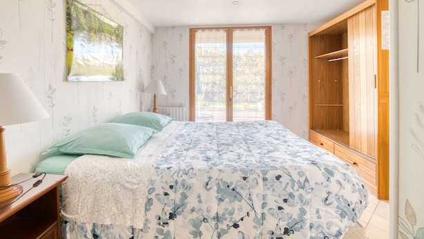 Une chambre à coucher avec un lit, une table de chevet, une lampe, une armoire et une fenêtre donnant sur un beau paysage.