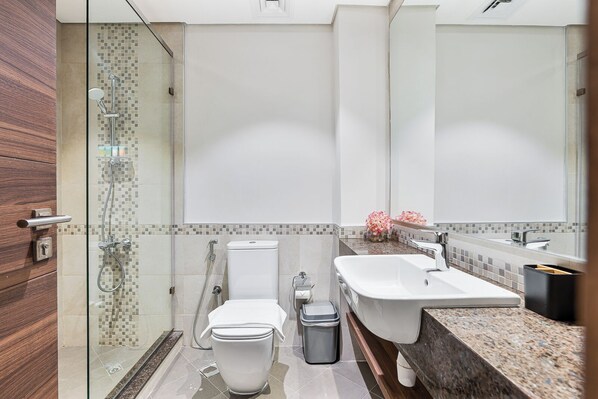 A modern bathroom with a glass-enclosed shower, a toilet, a sink, and a trash bin.
