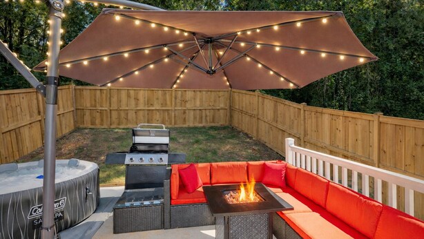 Un jardin avec un jacuzzi, un barbecue et un espace salon extérieur aménagé sous une tonnelle.