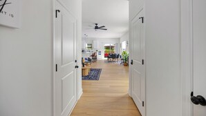 Un couloir avec des portes blanches, un ventilateur de plafond et un coin repas avec une table et des chaises.