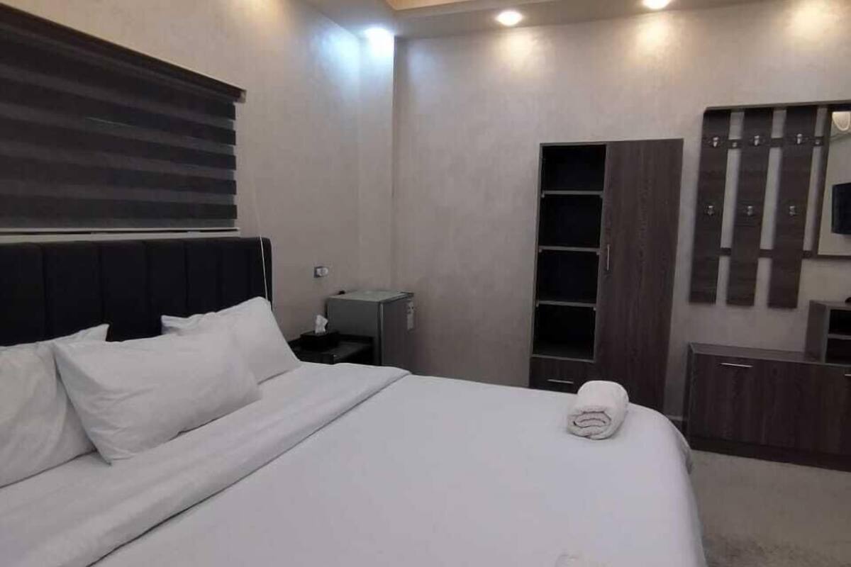 A modern bedroom with a large bed, built-in headboard, bedside tables, and a wardrobe.