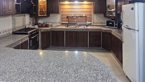 A kitchen with granite countertops, dark wooden cabinets, a white refrigerator, and a built-in oven. - hadrian's arch (Jerash)