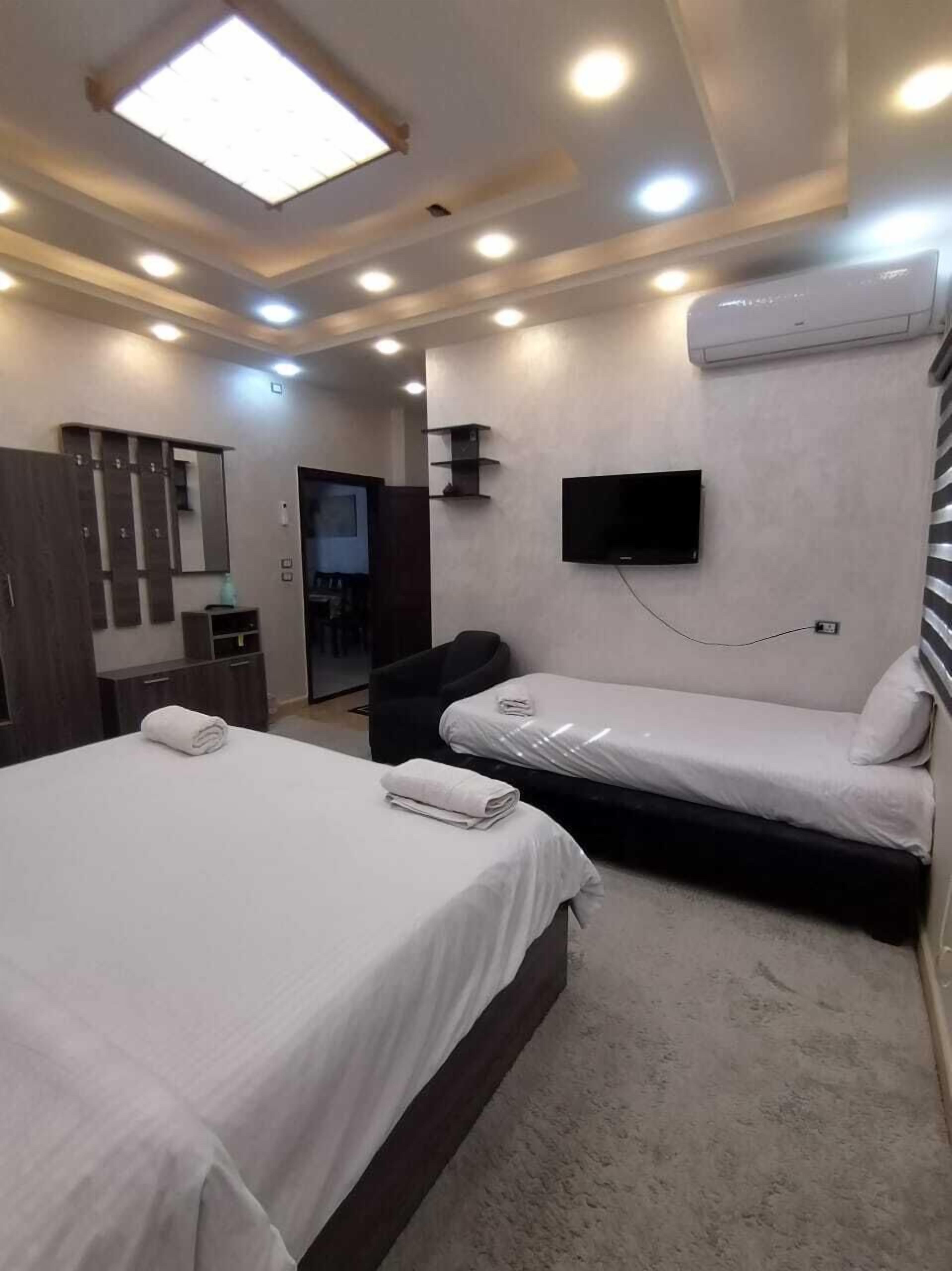 A hotel room with two beds, a flat-screen TV mounted on the wall, a ceiling light, and a built-in air conditioning unit.