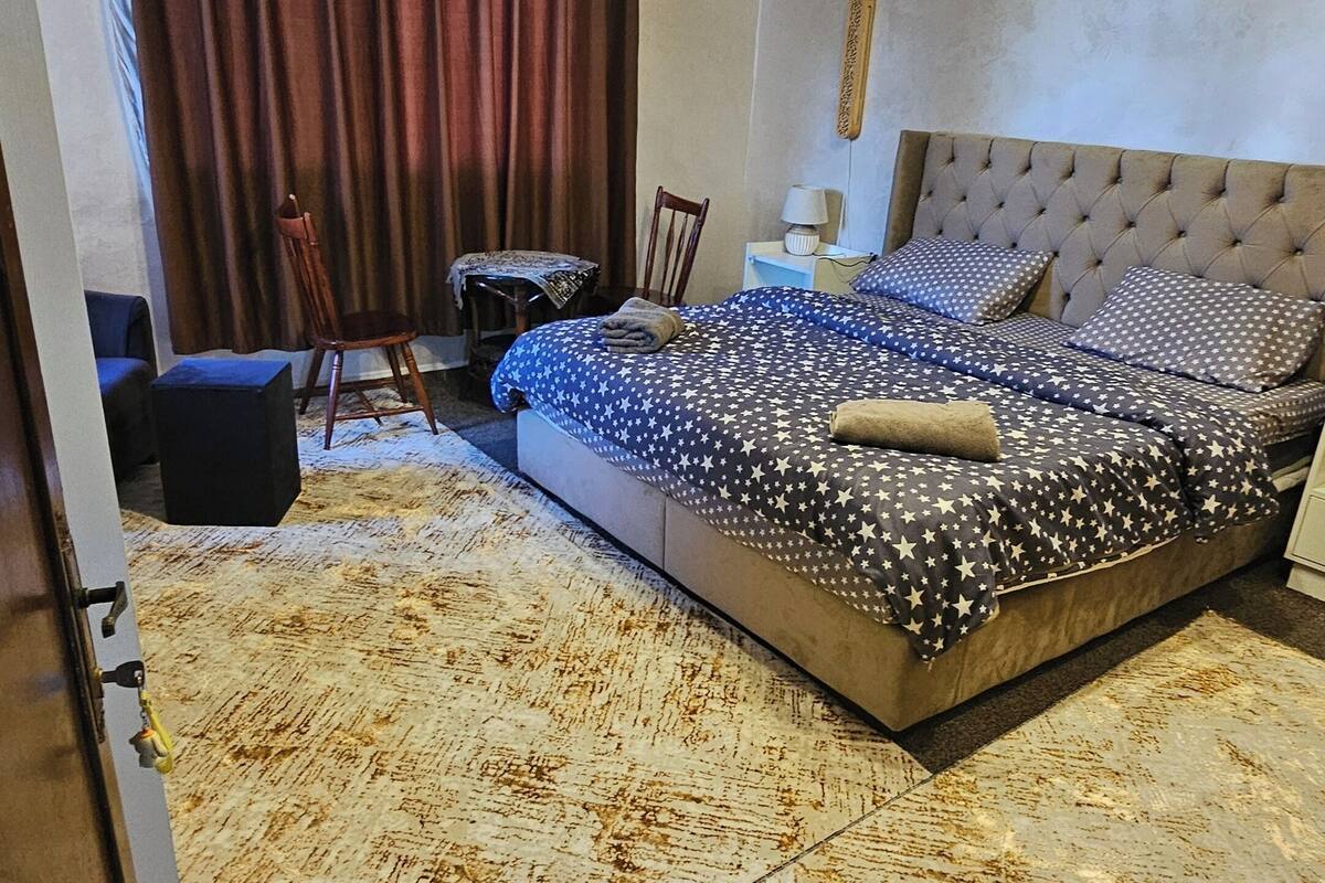 A bedroom with a large bed, a chair, a small table, and a curtain.