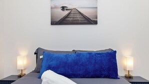 A bedroom with a bed, two bedside lamps, a blue pillow, and a white towel. - Uptown Retreat Sleeps 10 w/Hot Tub, Games /Fenced (Charlotte)