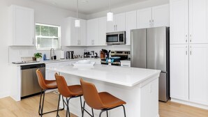 A modern kitchen with white cabinets, stainless steel appliances, a central island with bar stools, and pendant lighting. - Uptown Retreat Sleeps 10 w/Hot Tub, Games /Fenced (Charlotte)