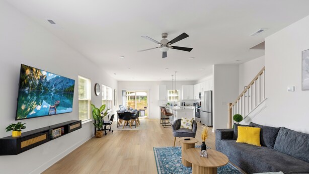 A spacious living area with a large TV, a ceiling fan, a dining area, and a kitchen in the background. - Uptown Retreat Sleeps 10 w/Hot Tub, Games /Fenced (Charlotte)