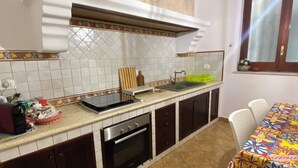 A kitchen with a tiled backsplash, a built-in oven, a sink, and a dining area with a table and chairs. - SAMPOLO70 APARTMENTS (Palermo)