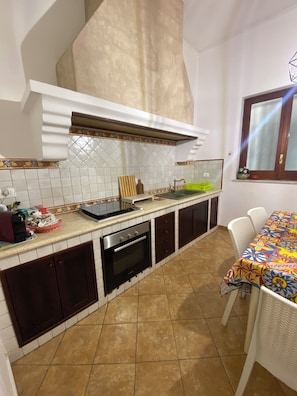 Une cuisine avec un mur recouvert de carreaux, un four encastré, un évier et un coin repas comprenant une table et des chaises.