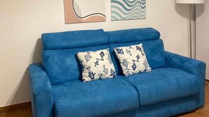 A blue sofa with two patterned cushions, a floor lamp, and two abstract wall art pieces. - SAMPOLO70 APARTMENTS (Palermo)