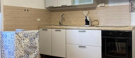 Une cuisine avec des armoires blanches, une hotte de cuisinière en acier inoxydable, un four encastré et une nappe à motifs posée sur le comptoir.