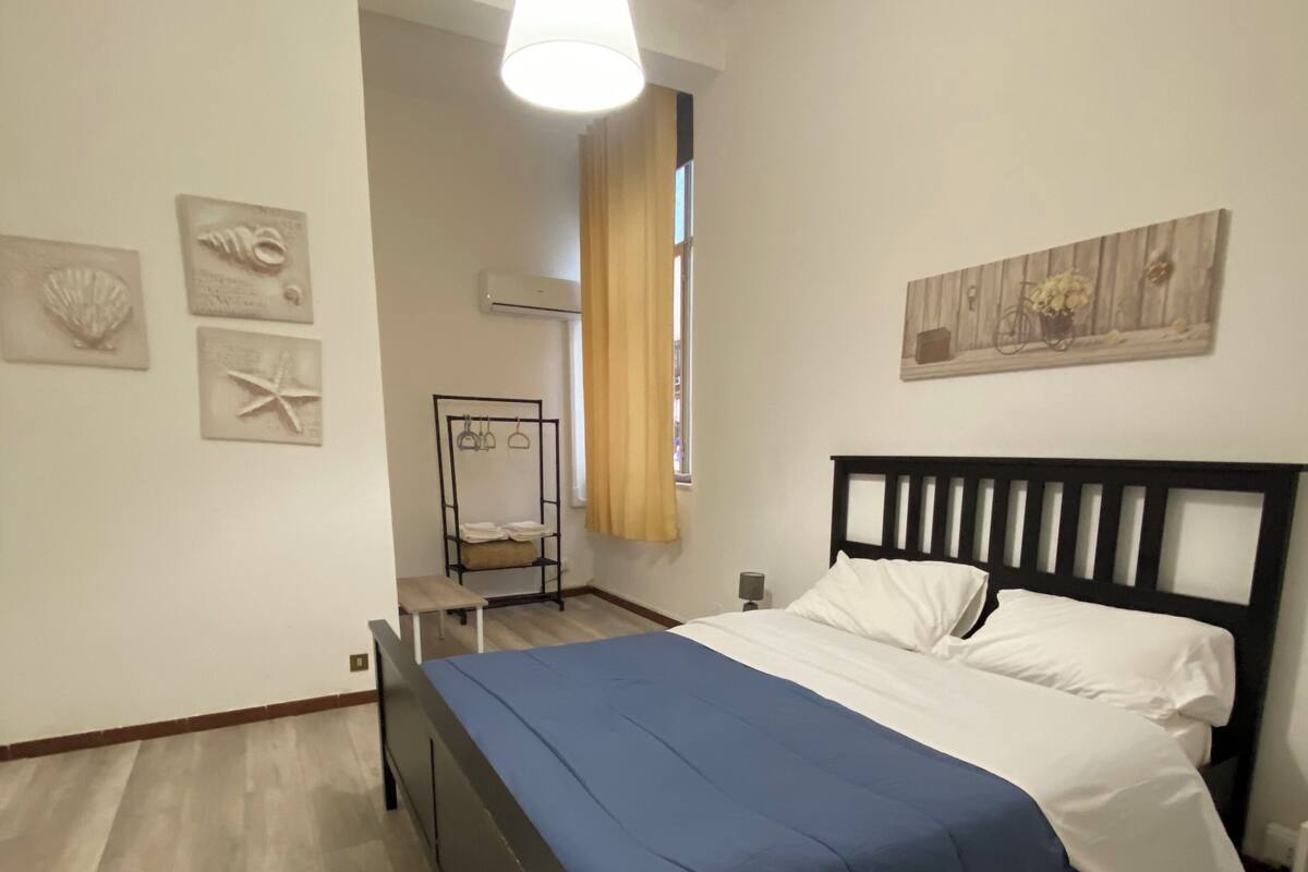 Un dormitorio con cama, lámpara colgante, ventana con cortinas y adornos en la pared.