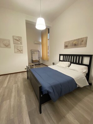 Quarto com cama, luminária pendente, janela com cortinas e decorações nas paredes.