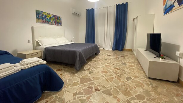 A hotel room with a bed, a bedside table with a lamp, a TV on a stand, and a painting on the wall. - SAMPOLO70 APARTMENTS (Palermo)