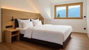 A modern bedroom with a large bed, a wooden headboard, a nightstand, and a window with a mountain view.